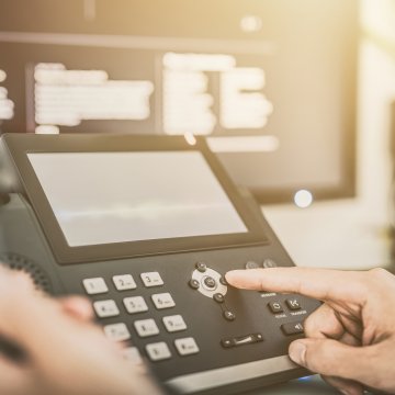 best voip systems services dialing on voip phone office computer monitor in the background